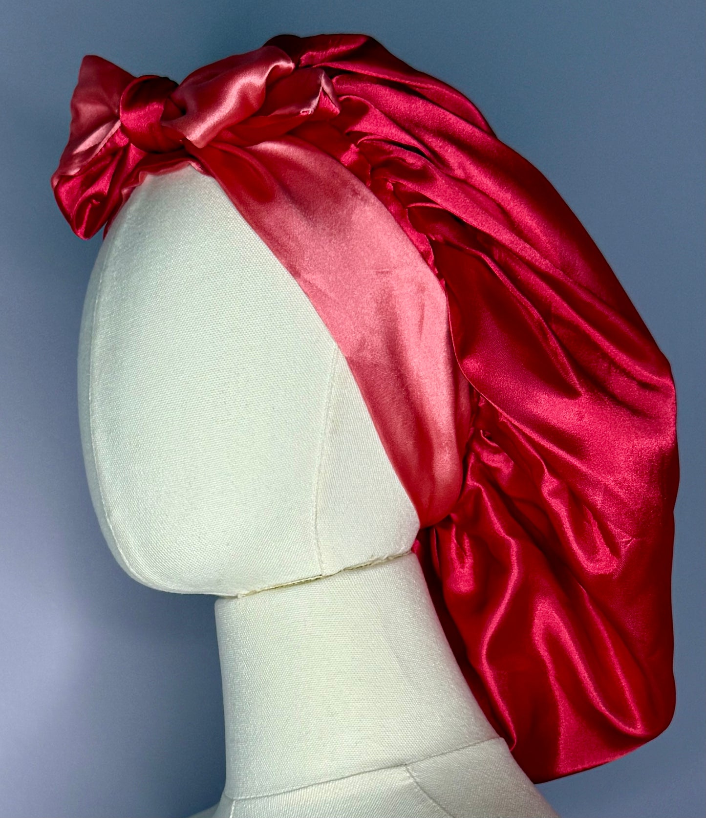 Double layer reversible satin hair bonnet with long ties to adjust comfort in pink and res colors.