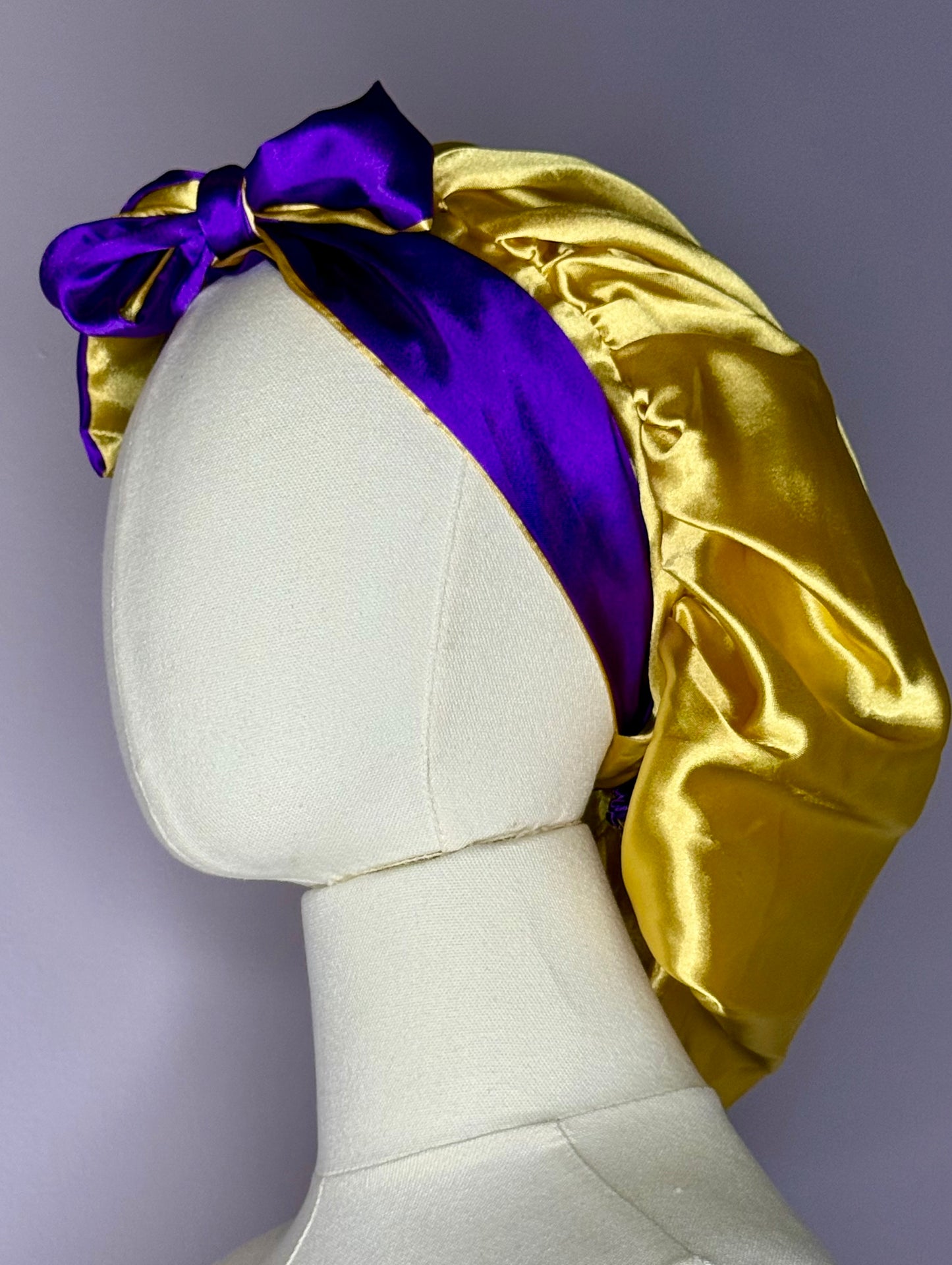 Double layer reversible satin hair bonnet with long ties to adjust comfort in purple and gold colors. 