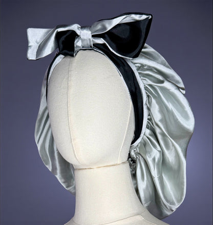 AQueenzDen double layer reversible satin bonnet in silver and black with adjustable ties and a large bow accent.