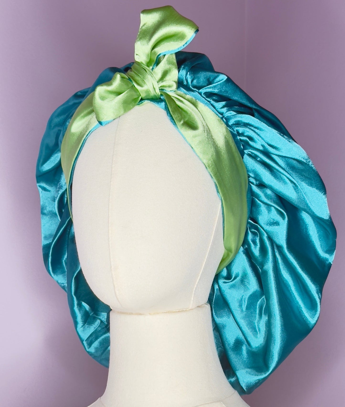 AQueenzDen reversible double layer satin bonnet in teal and lime green with adjustable ties tied in a bow.