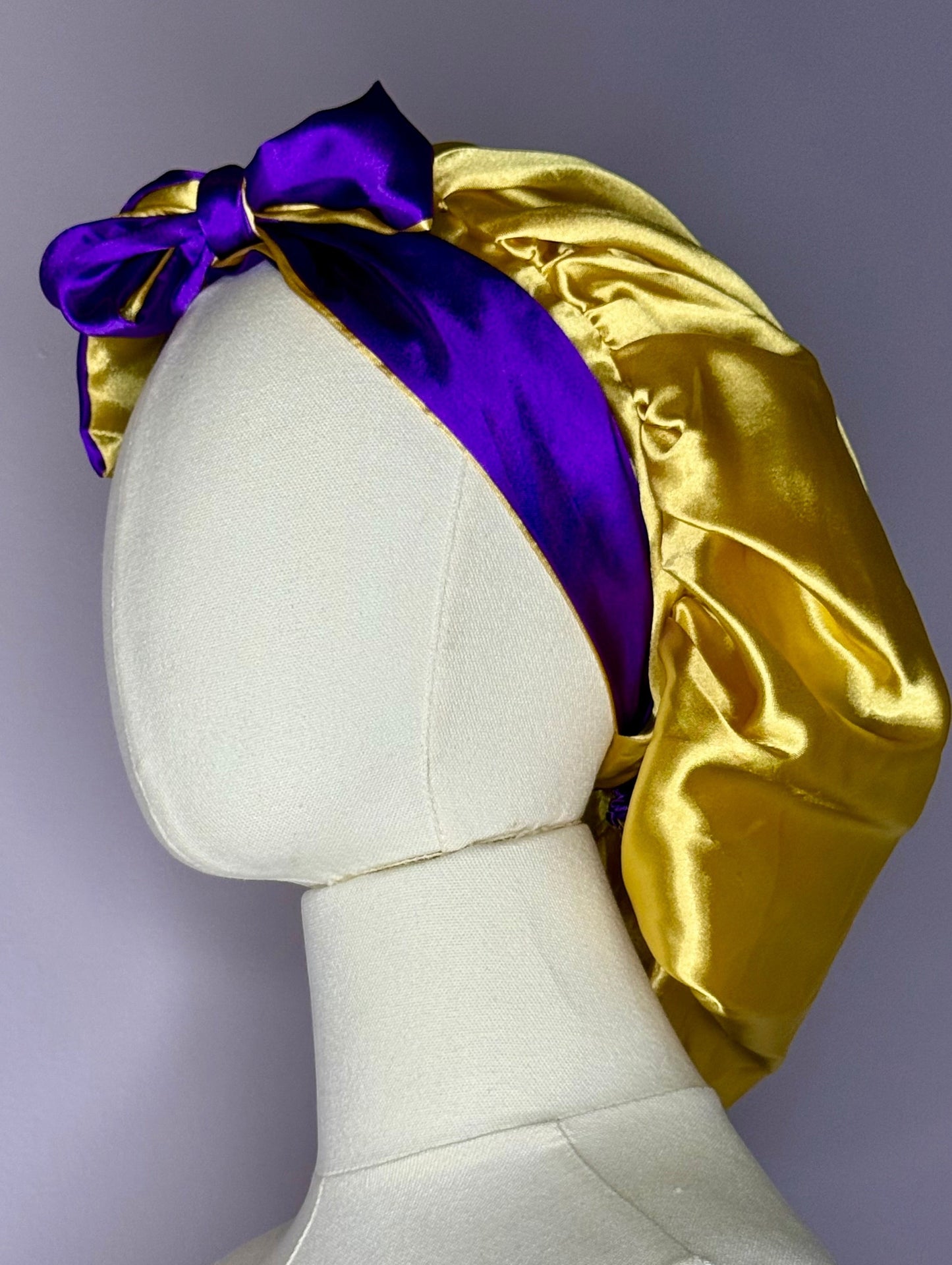 AQueenzDen gold and purple double layer satin bonnet with adjustable ties and a bow detail.