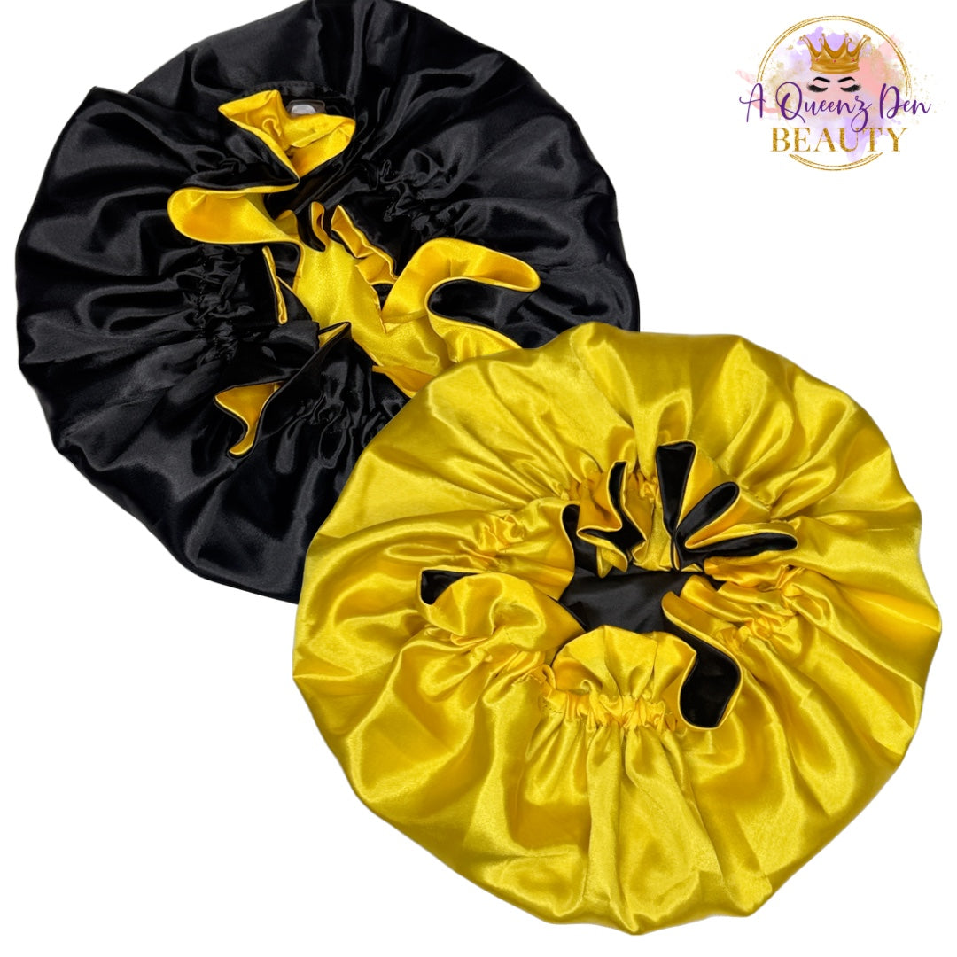 A Queenz Den reversible satin bonnet in black and yellow, featuring an adjustable tie closure for a secure fit.