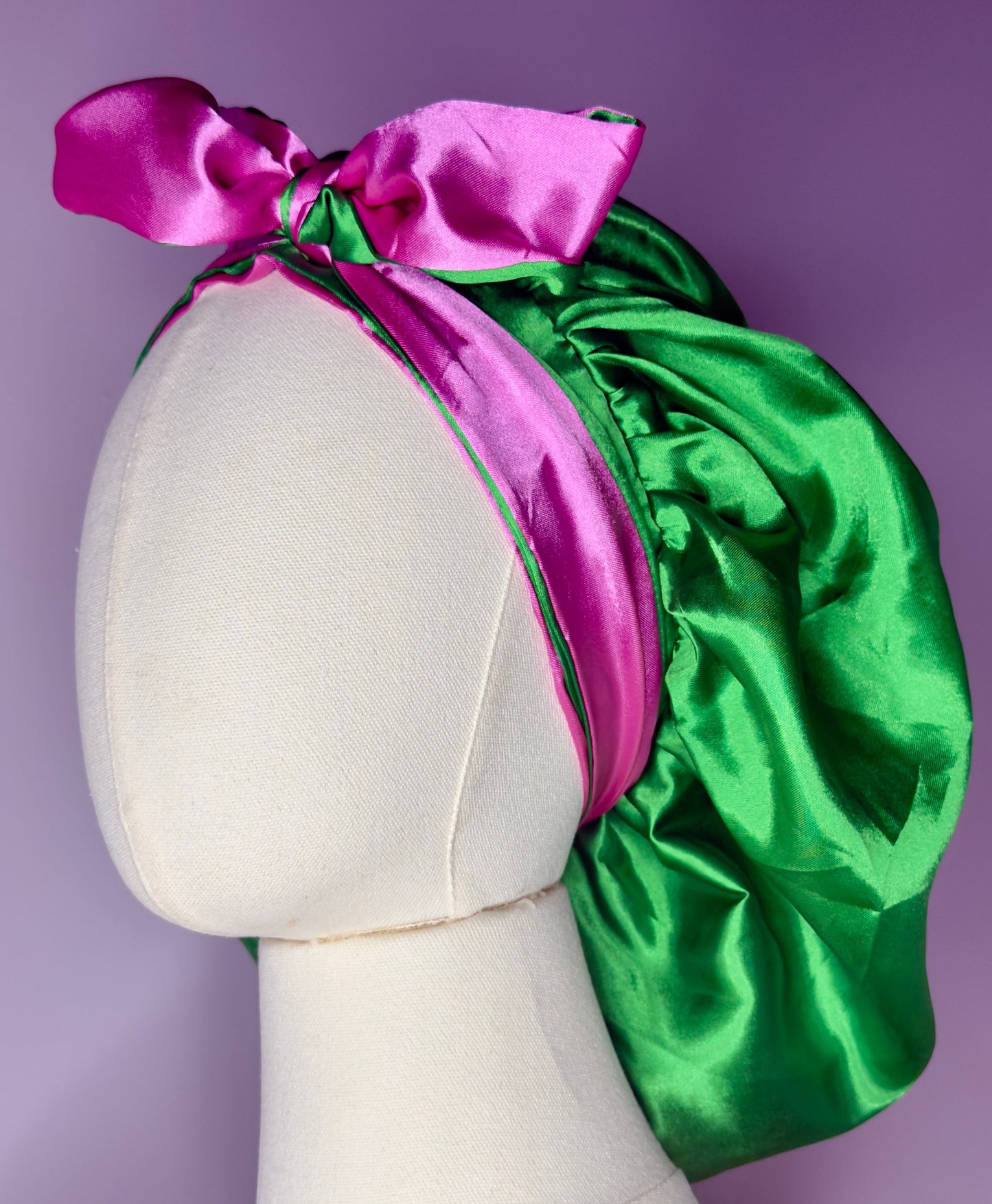 AQueenzDen reversible satin bonnet in green with a pink trim and bow. Features adjustable ties for a secure fit.